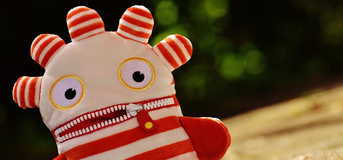 A red-and-white soft toy with bewildered eyes and a half-zipped mouth.